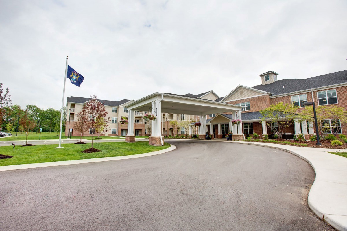 A large building with a covered entrance and a driveway, featuring landscaping and a flagpole.