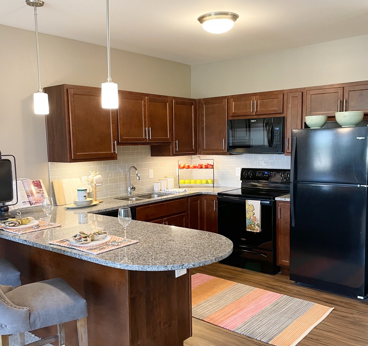 A modern kitchen with dark wood cabinets, a black refrigerator and stove, and an island counter with pendant lighting.