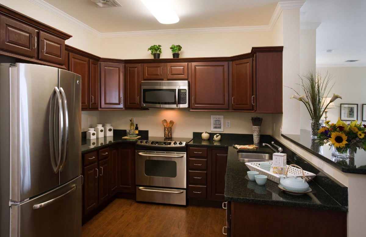A modern kitchen with wood cabinets, stainless steel appliances, and green countertops.