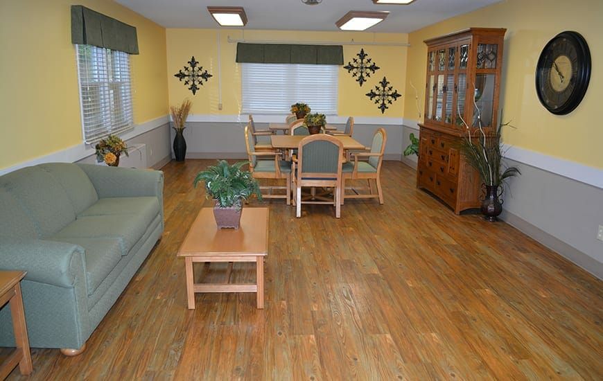 A cozy dining and living room area with wooden flooring, featuring a table and chairs, a cabinet, and indoor plants for decoration.