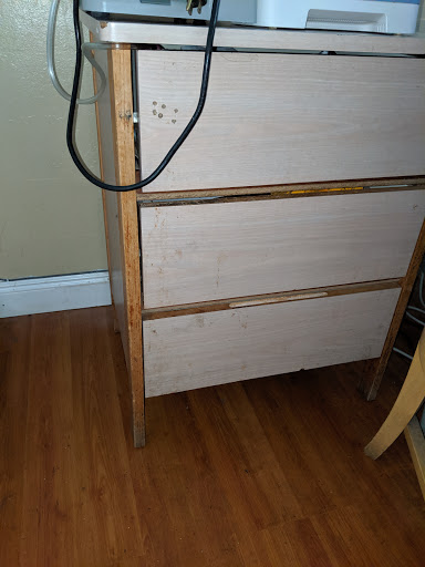 A wooden dresser with a minimal design, showcasing its drawers and standing on a hardwood floor.