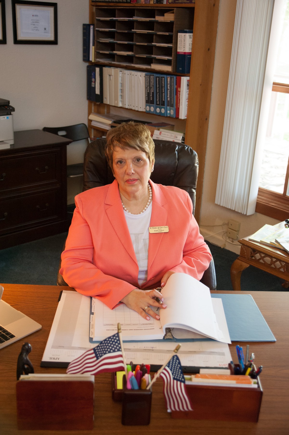 A woman seated at her desk in an office, surrounded by books and documents.