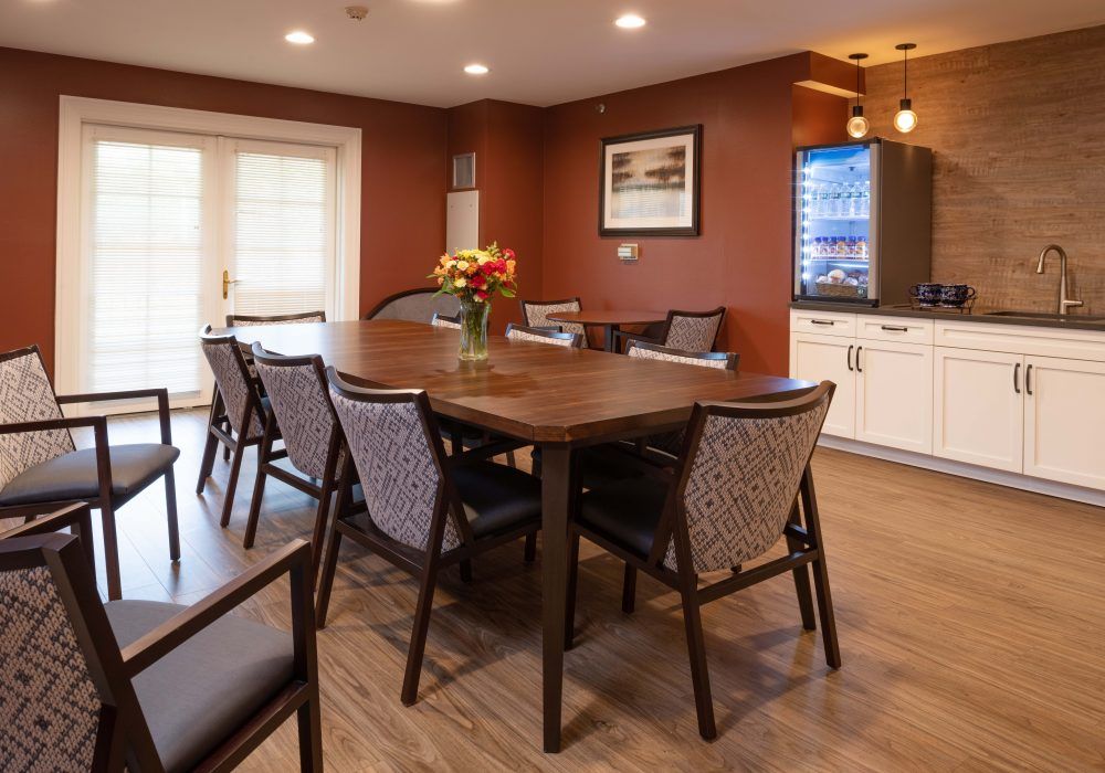 A cozy dining room with a large wooden table and chairs, decorated with flowers.