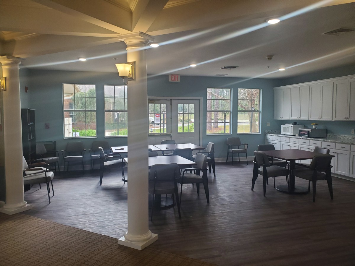 A spacious and well-lit dining area with tables and chairs, adjacent to a kitchenette.