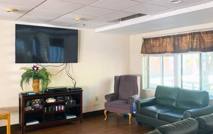 A cozy living room setup with a television mounted on the wall, accompanied by a couch, armchair, and entertainment center.