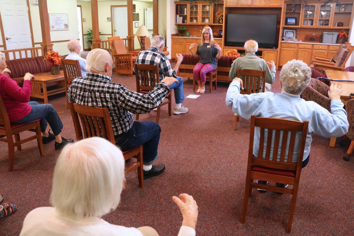 A group of senior citizens participating in a seated exercise class at a community center.
