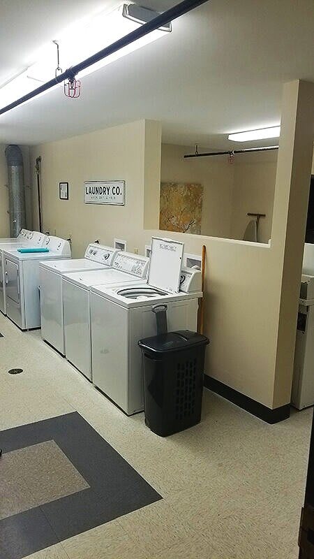 A spacious laundry room with multiple washing machines and a trash can.