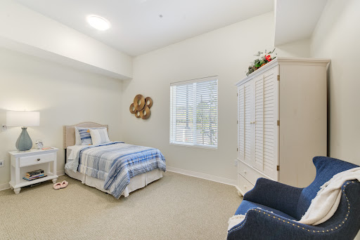A cozy and well-lit bedroom featuring a single bed with blue and white bedding, complemented by a decorative wardrobe and natural light from the window.