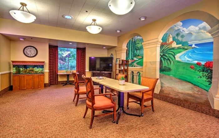 A warmly lit room with a table and chairs, featuring a colorful mural on the wall.