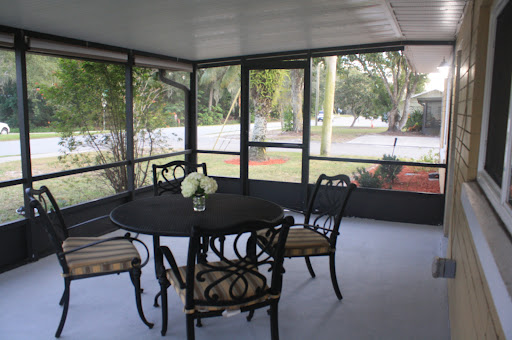 A cozy screened porch featuring a round table with elegant chairs and decorative flowers, perfect for enjoying natural light.