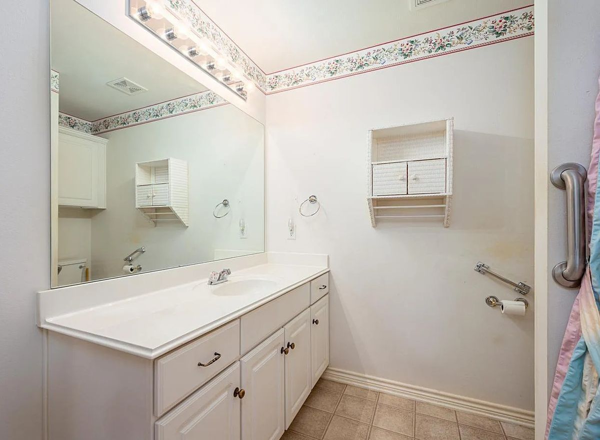 A clean bathroom with a large mirror, white vanity, and decorative wall border.