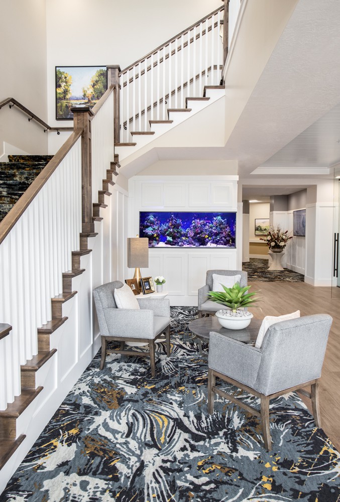 A modern living room with a staircase, featuring stylish chairs and a large aquarium as a focal point.