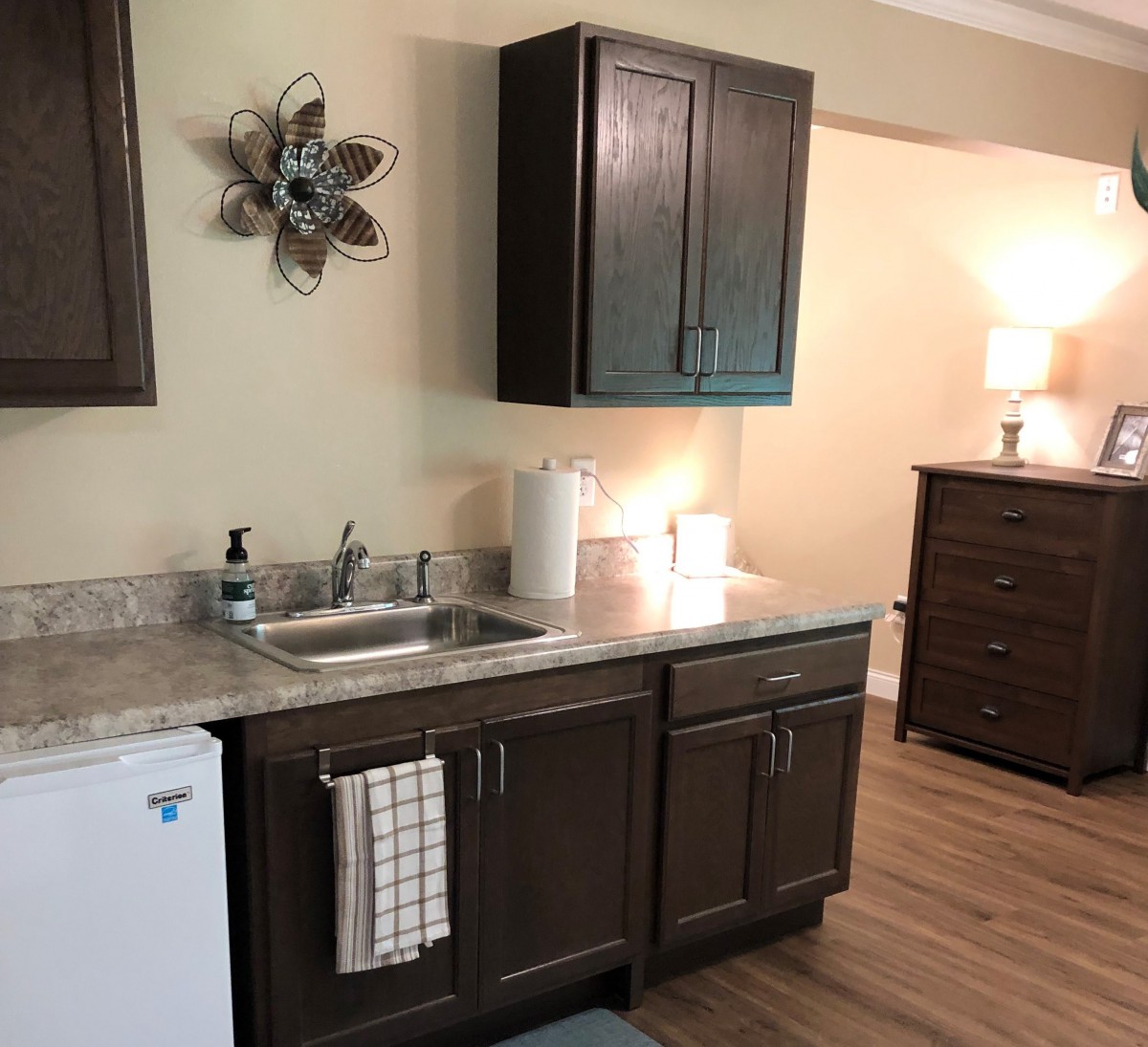 A small kitchenette with a sink, cabinets, and countertop in a cozy room setting.