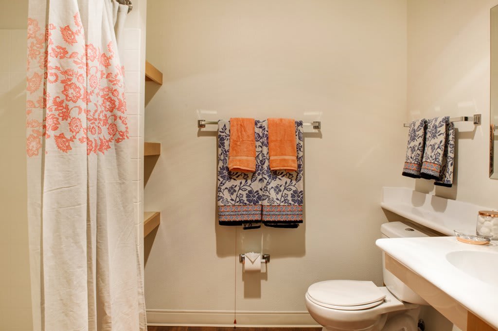 A neatly organized bathroom with colorful towels and a patterned shower curtain.