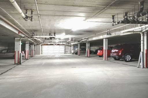 An empty parking garage with a few cars under bright overhead lights.