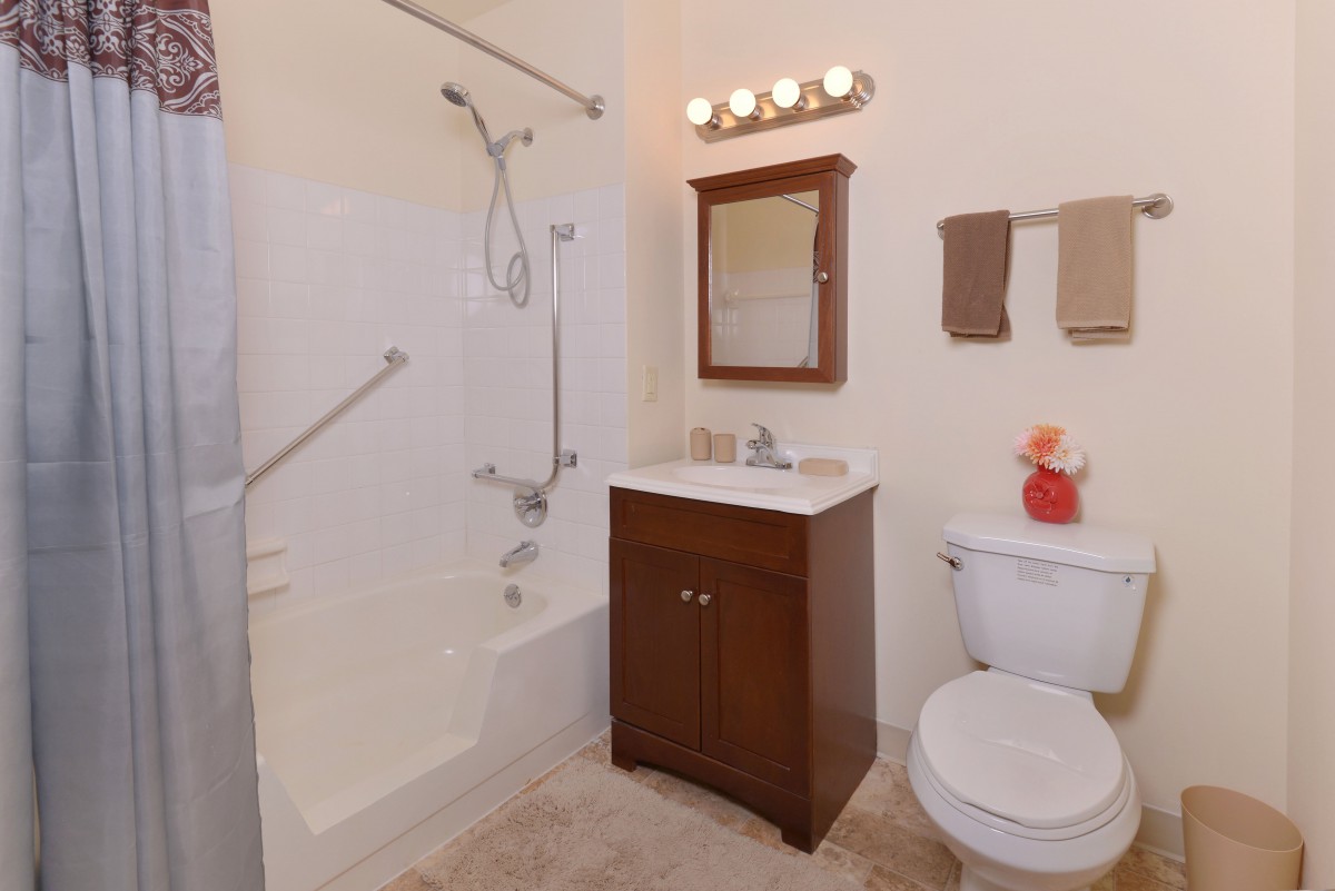 A modern bathroom featuring a shower and bathtub combination, a wooden vanity with a mirror, and a toilet.