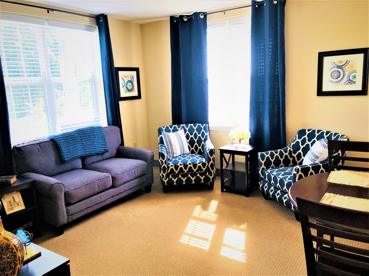 A cozy living room with a sofa, patterned armchairs, and blue curtains.