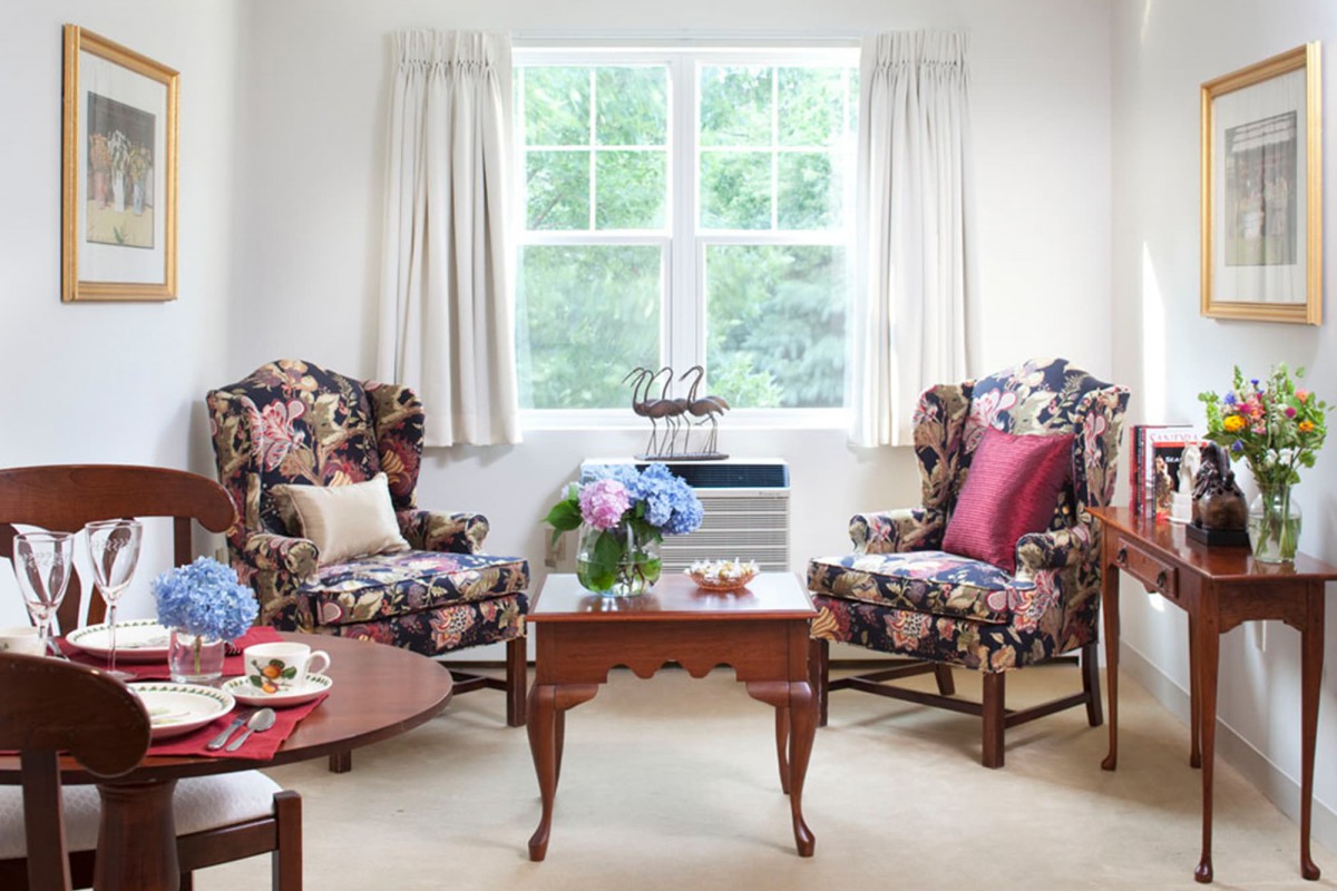 A cozy living room with floral armchairs and a wooden coffee table, accented by decorative pillows and a vase of hydrangeas.