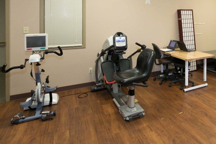 A healthcare facility room featuring exercise and rehabilitation equipment, including indoor bikes.