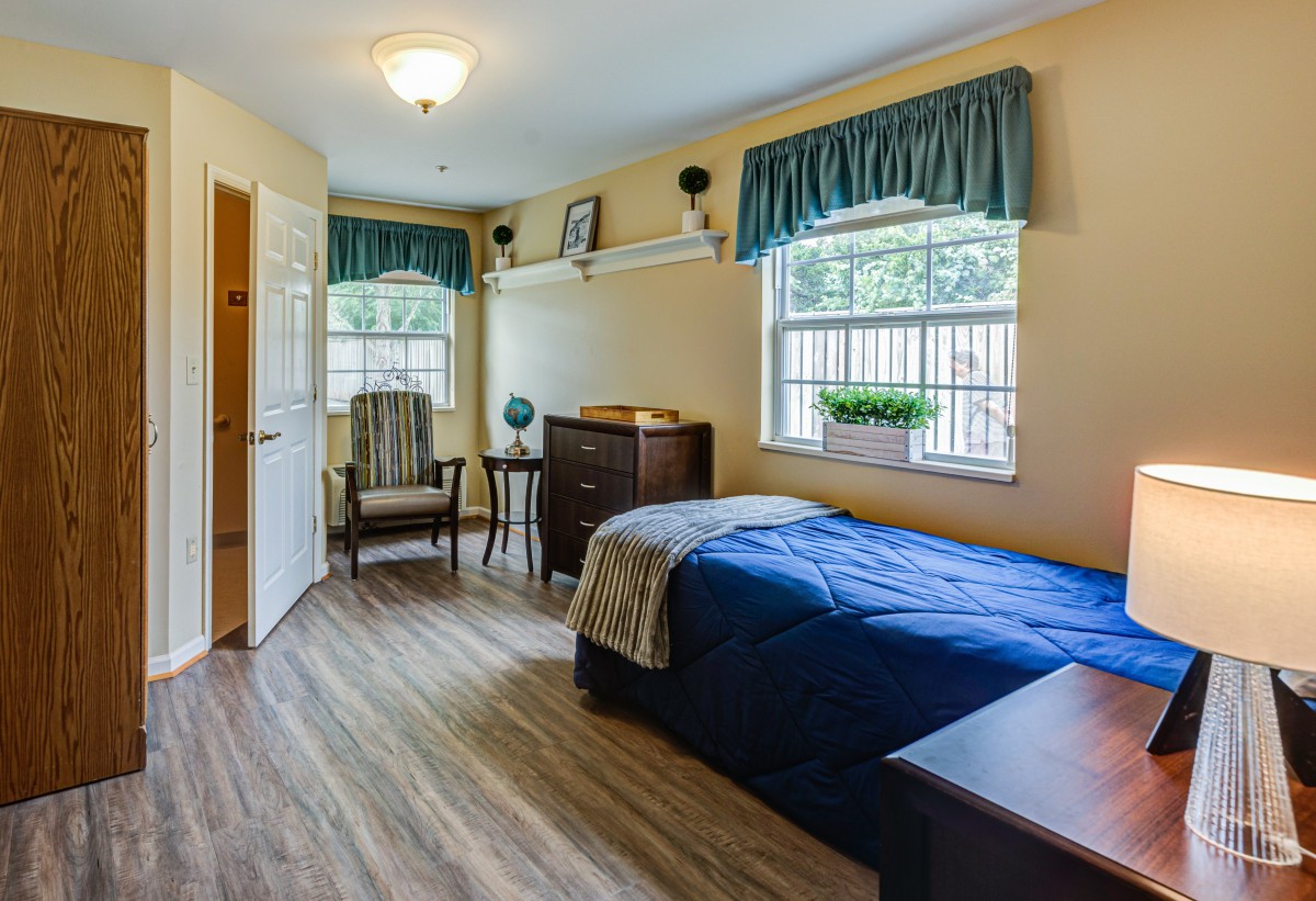 A cozy bedroom with a single bed, wooden furniture, and large windows letting in natural light.