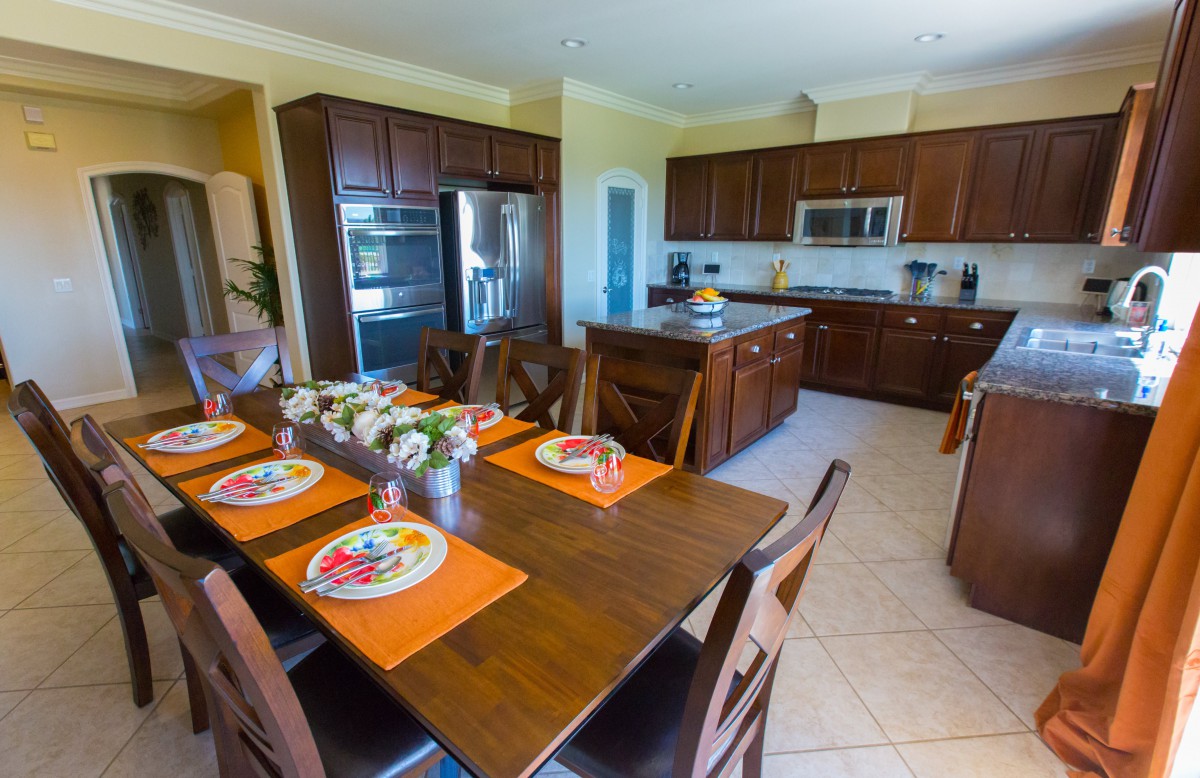 A modern kitchen and dining area with a wooden table set for a meal, featuring warm wood cabinetry and stainless steel appliances.