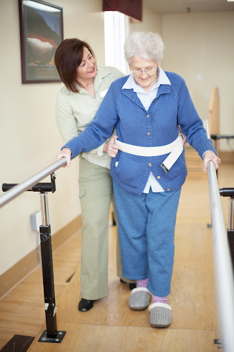 A caregiver assists an elderly woman as she practices walking using support rails.