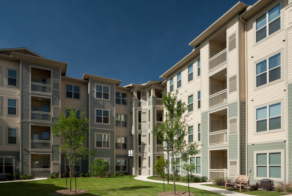 A modern apartment building with balconies and a landscaped courtyard on a sunny day.