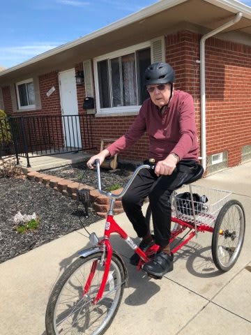 An elderly man wearing a helmet rides a red tricycle in a residential area.