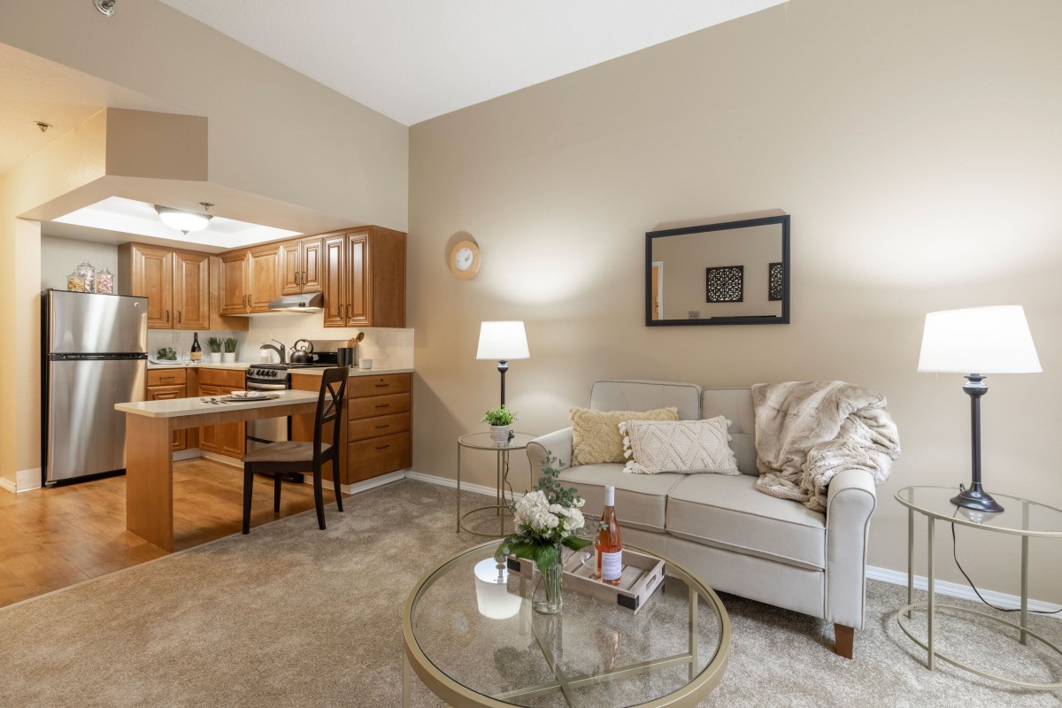 A cozy living room with a comfortable sofa, glass coffee table, and adjacent kitchen area.