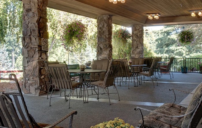 A cozy patio with stone pillars, featuring outdoor seating and hanging plants.