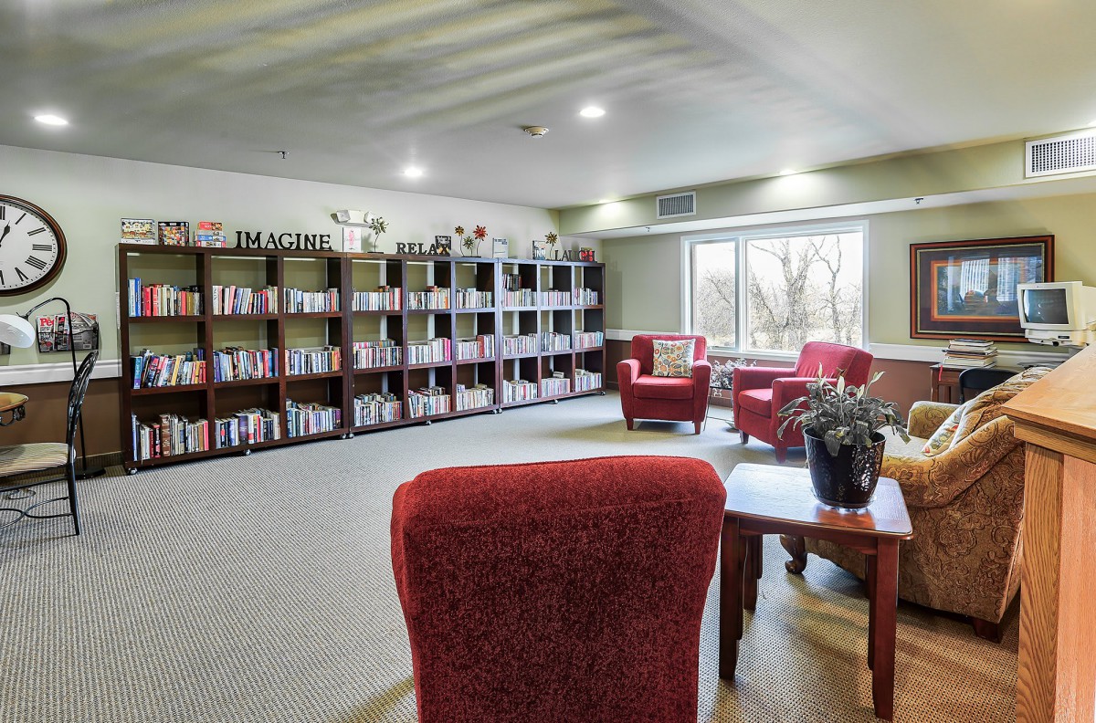 A cozy library with red chairs and bookshelves filled with books, offering a bright reading area by the window.