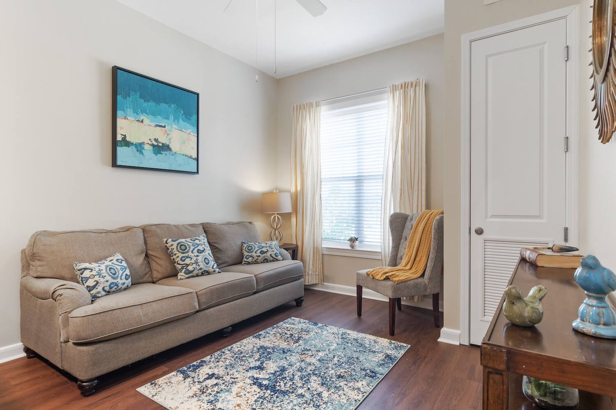 A cozy living room with a sofa, armchair, and decorative elements like a painting and rug.