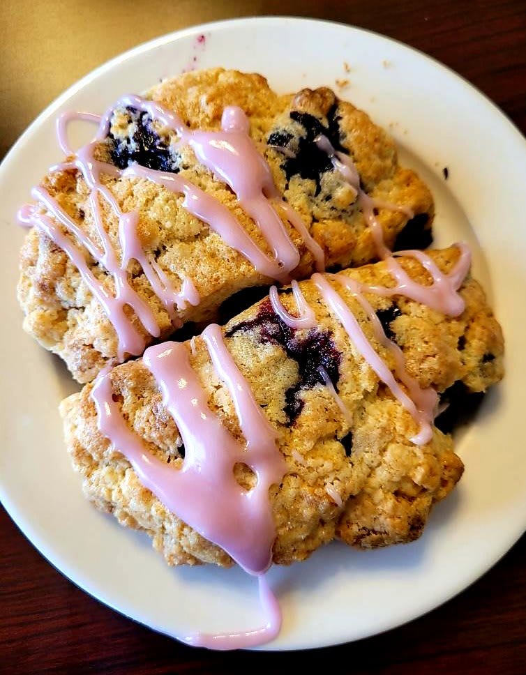 Blueberry scones with pink icing drizzle on a white plate.