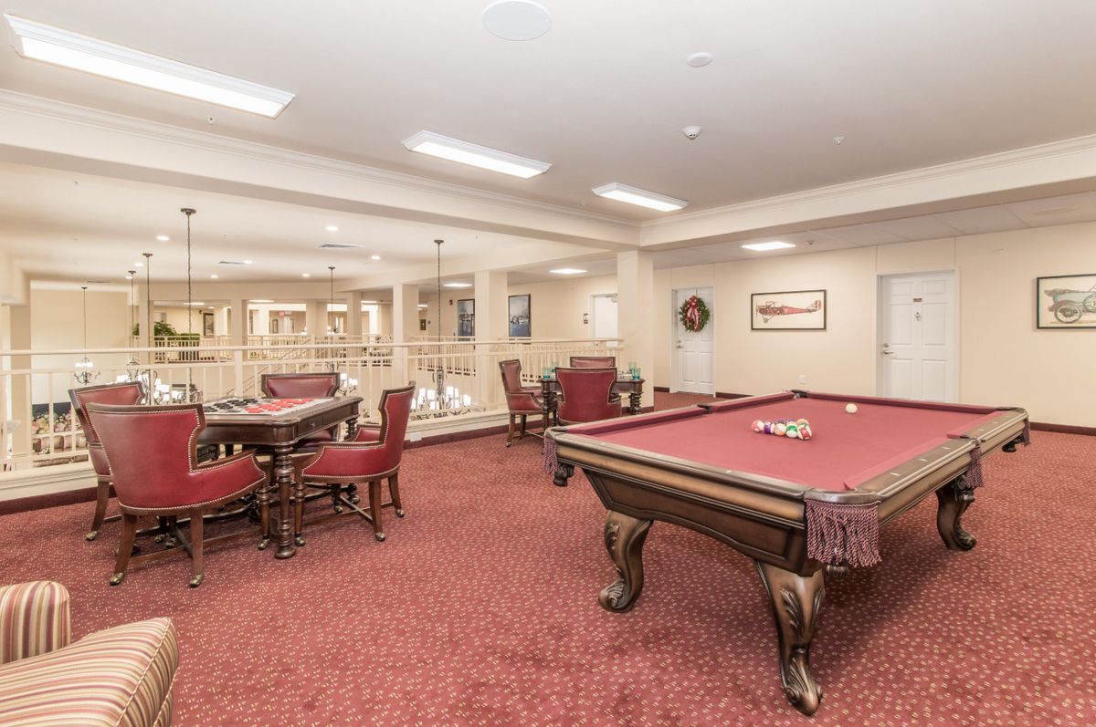 A spacious game room featuring a pool table and seating area with red carpet flooring.