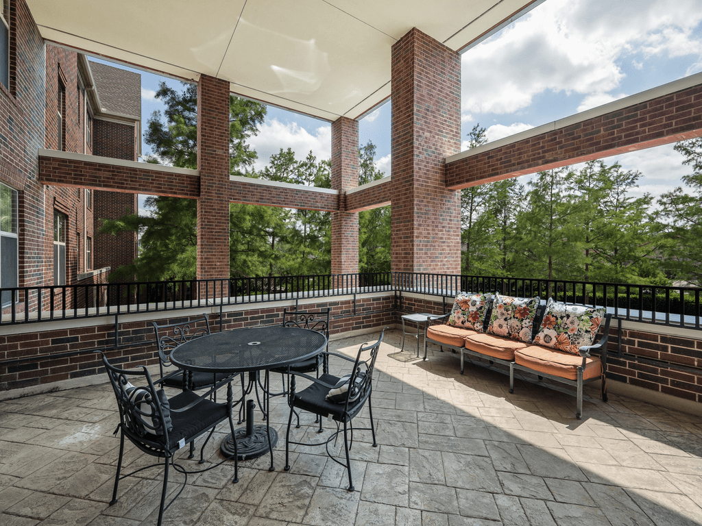 A spacious outdoor patio with a table, chairs, and a sofa surrounded by brick pillars and greenery.