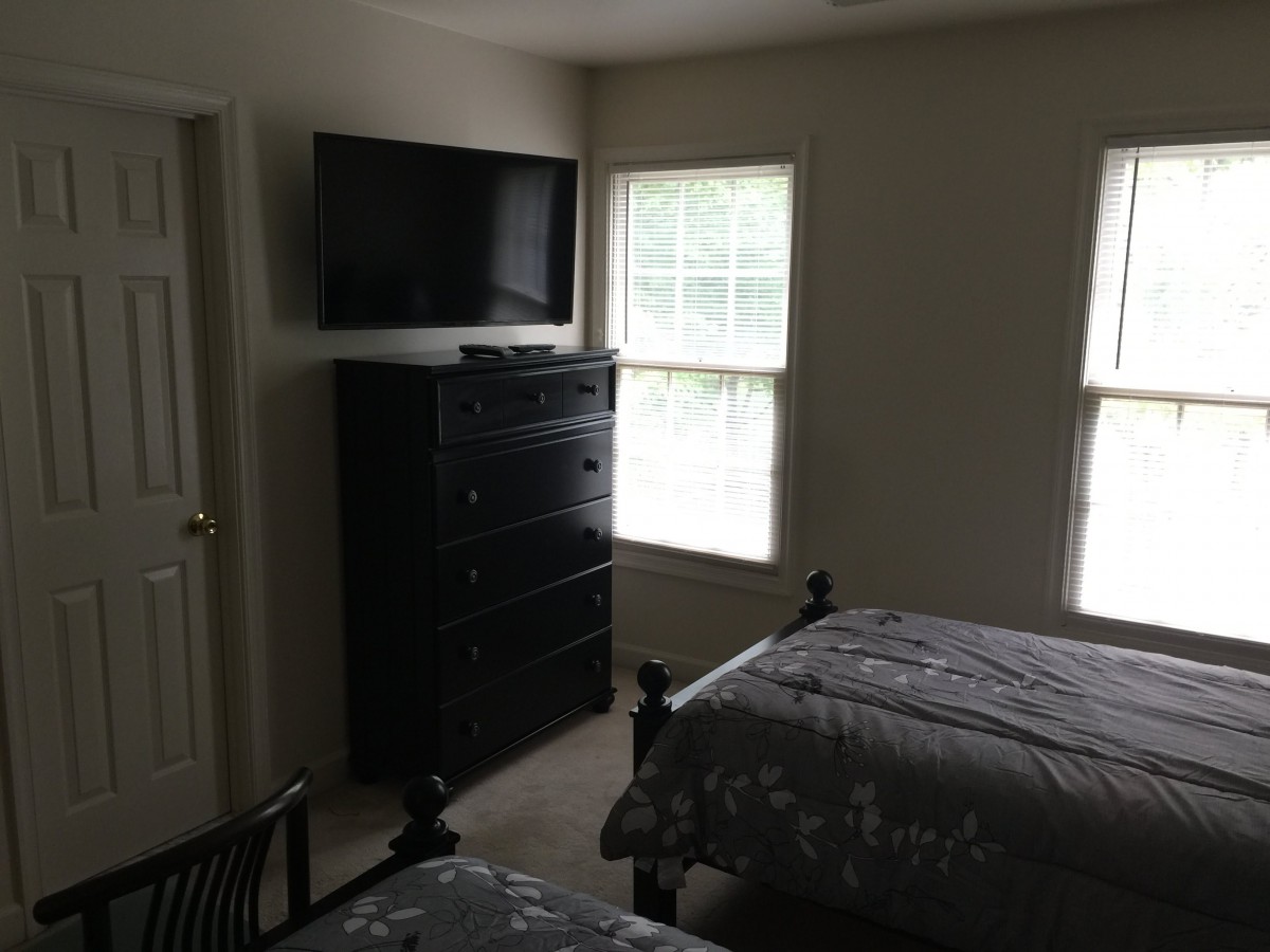 A bedroom with two twin beds, a wall-mounted TV, and large windows.