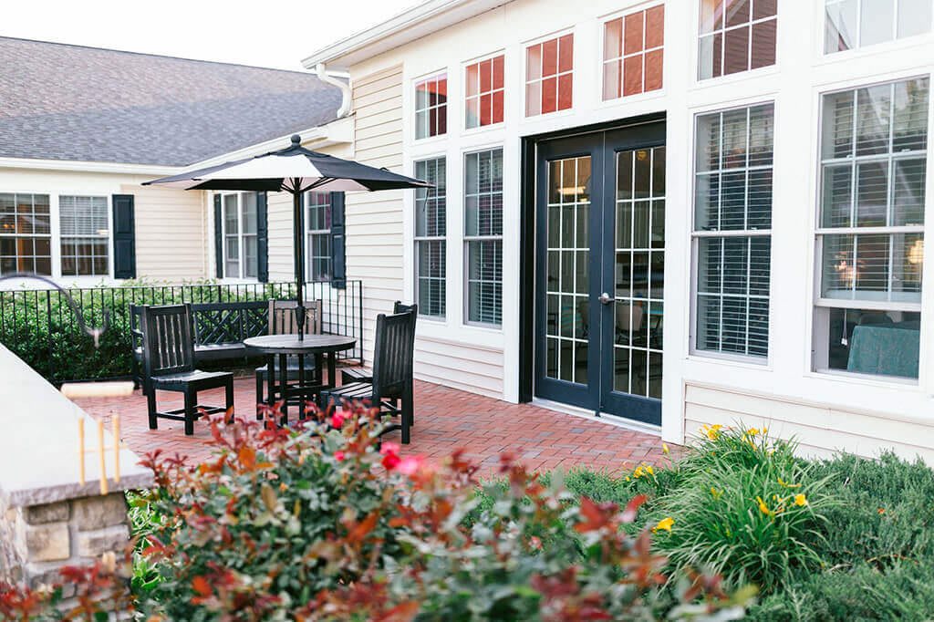 A cozy patio area featuring outdoor seating with an umbrella, surrounded by a garden with vibrant flowers.