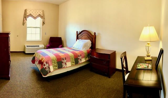 A cozy bedroom with a single bed, wooden furniture, and a colorful quilt.