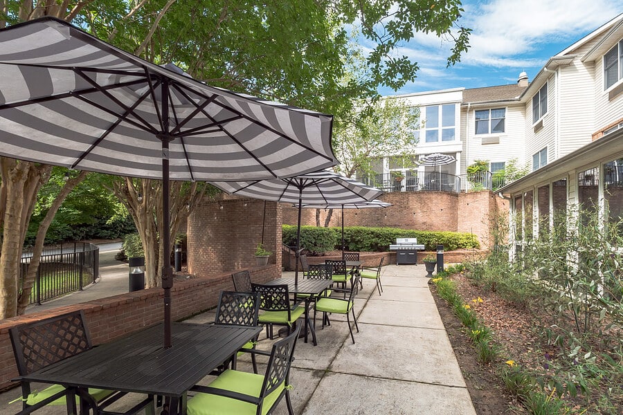 A well-maintained outdoor patio with tables and chairs under striped umbrellas, surrounded by greenery and a brick wall.