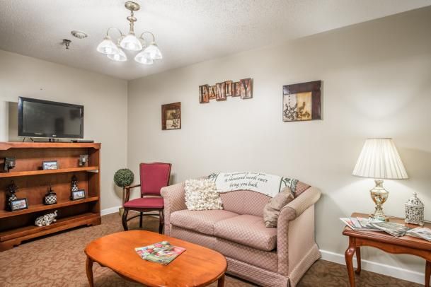 A cozy living room with a sofa, armchair, and coffee table, decorated with wall art and a bookshelf.
