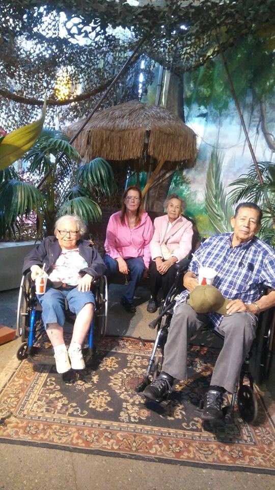 A group of four people posing in front of a tropical-themed backdrop, with two seated in wheelchairs.