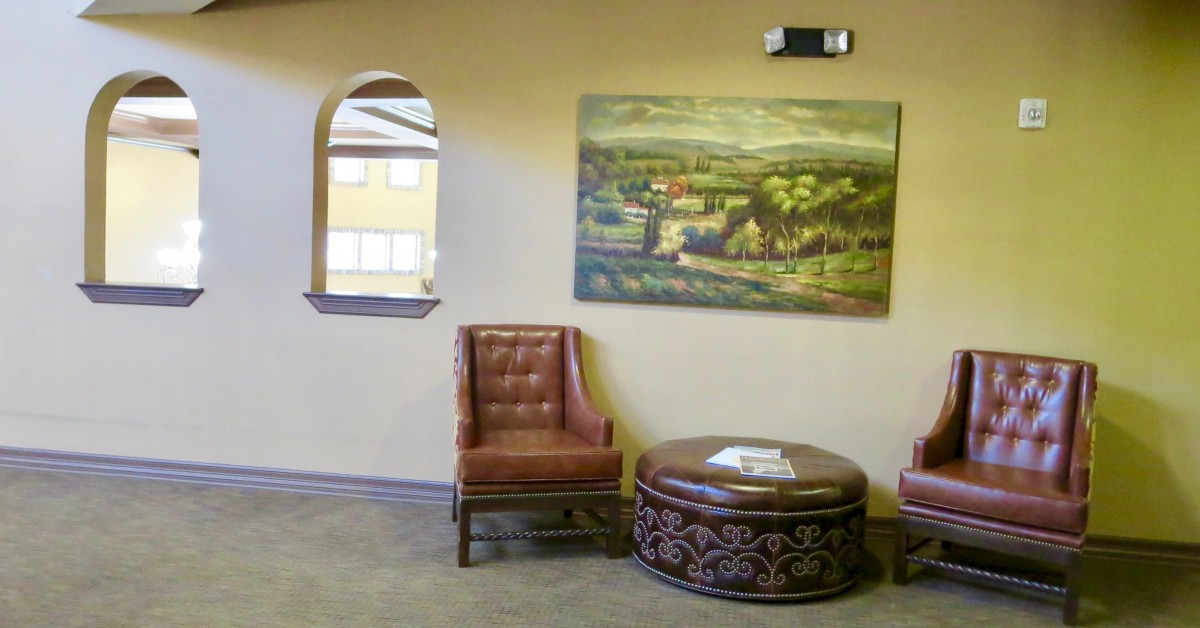 A cozy seating area with a leather chair, decorative round table, and landscape painting on the wall.