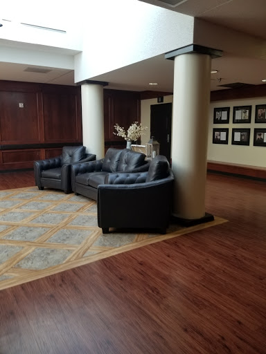 A cozy lobby area featuring black leather sofas and a warm wooden floor, accented by decorative columns and framed photographs on the wall.