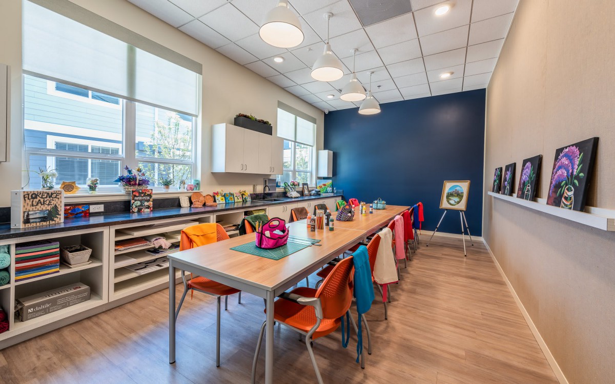 A modern art classroom with colorful chairs and backpacks, featuring large windows and a blue accent wall.