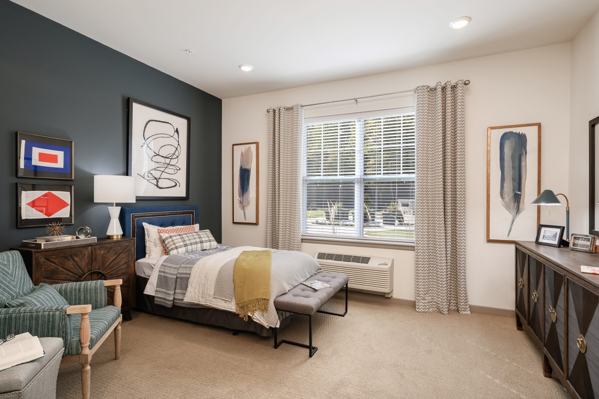 A modern bedroom featuring a stylish bed, large window with curtains, and contemporary artwork on the walls.
