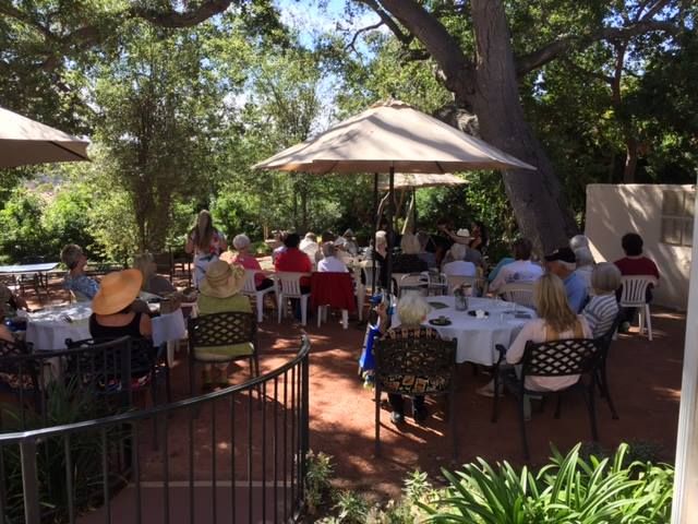People enjoying outdoor dining under umbrellas on a sunny patio.