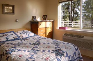 A cozy bedroom with a quilted bedspread and sunlight streaming through the window.