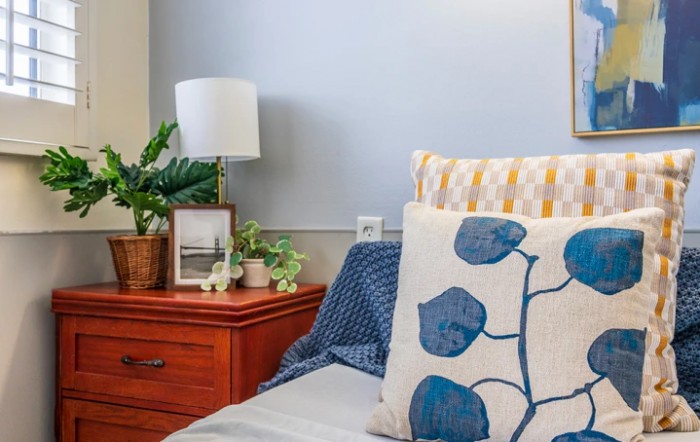 A cozy bedroom setting with a neatly arranged nightstand featuring a lamp, plants, and decorative pillows.