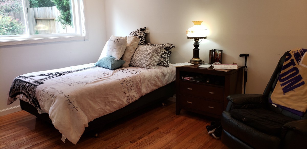 A cozy bedroom with a neatly made bed, featuring multiple pillows and a nightstand with a lamp.