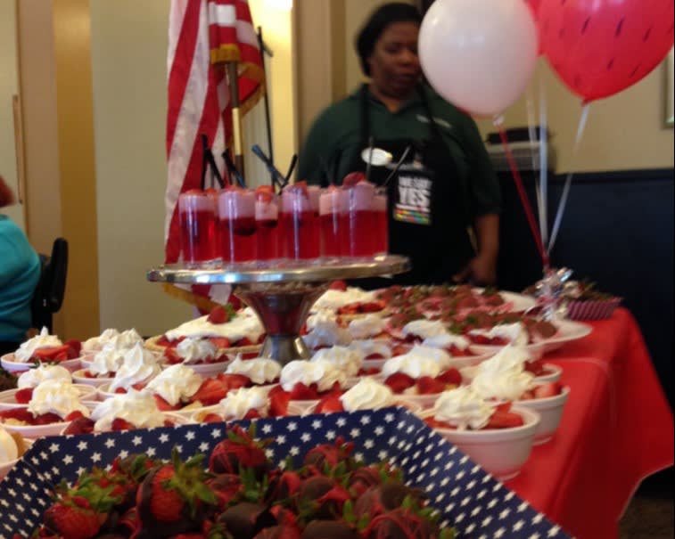 A festive dessert table adorned with various strawberry dishes and decorations, including balloons and a flag.